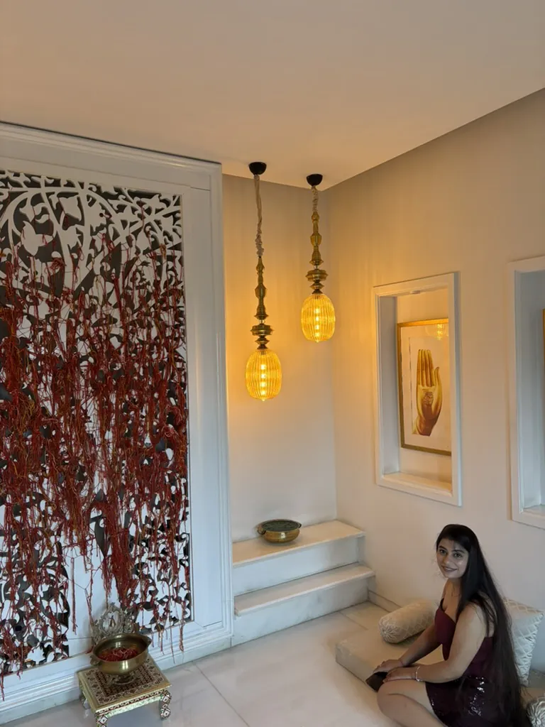 Divya in the prayer room under two glowing brass lamps