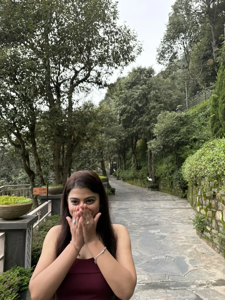Divya laughing behind her hands on a tree-lined path